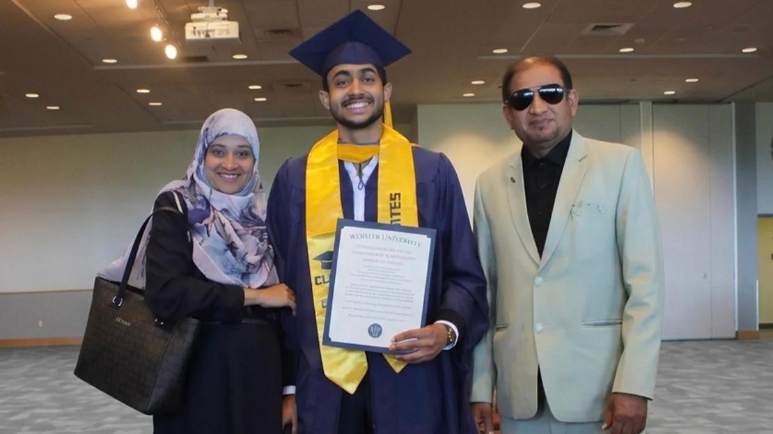 A graduate dressed in commencement attire poses for a photo with family.