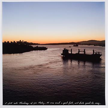 A sunset view over a wide body of water with the silhouette of a city skyline in the distance and a large cargo ship anchored on the right. A single line of white handwritten text runs along the bottom.