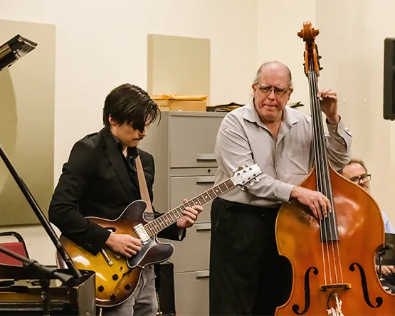 A student performing on guitar and accompanied by a professor on bass.