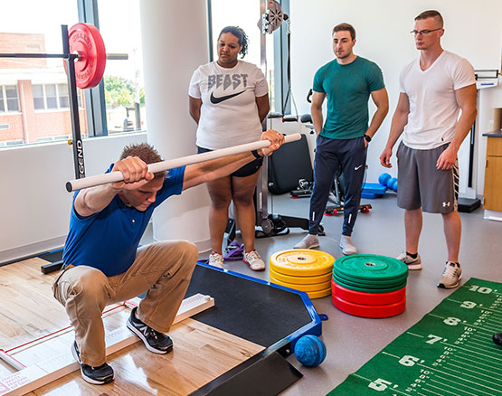 One instructor demonstrating exercises with weight bar equipment to several students