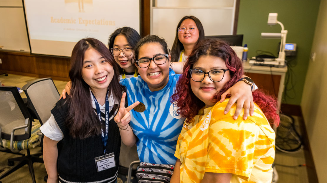 A group of Webster students smile and pose for a photo in a classroom.